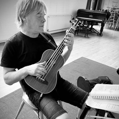 A bass ukulele player concentrating at rehearsal, songbook on the stand.