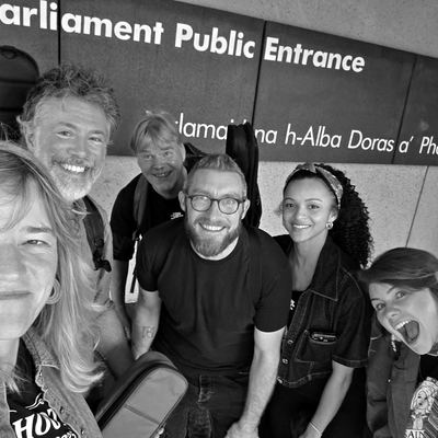 A band selfie under the Scottish Parliament public entrance sign.