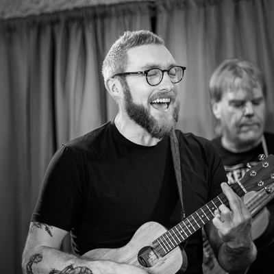 A ukulele player in glasses, beaming.