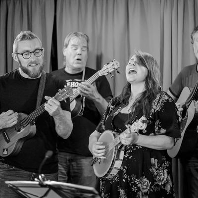 Four of the band singing out together, ukuleles and banjo up.